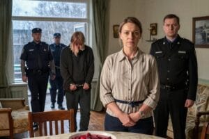 Жінка спокійно стоїть у вітальні, поки її чоловіка в кайданках виводить поліція, брат-прокурор поруч.