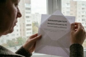 Жінка у звичайній квартирі тримає конверт і дивиться на результат ДНК-тесту на батьківство, де вказано ймовірність 0 відсотків