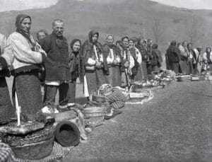 Українські селяни в автентичному одязі стоять у черзі біля пасхальних кошиків на освячення біля церкви 100 років тому. Старовинне чорно-біле фото.